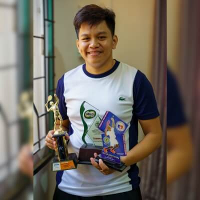 Coach Geo holding three trophies, showing champion status in three different events